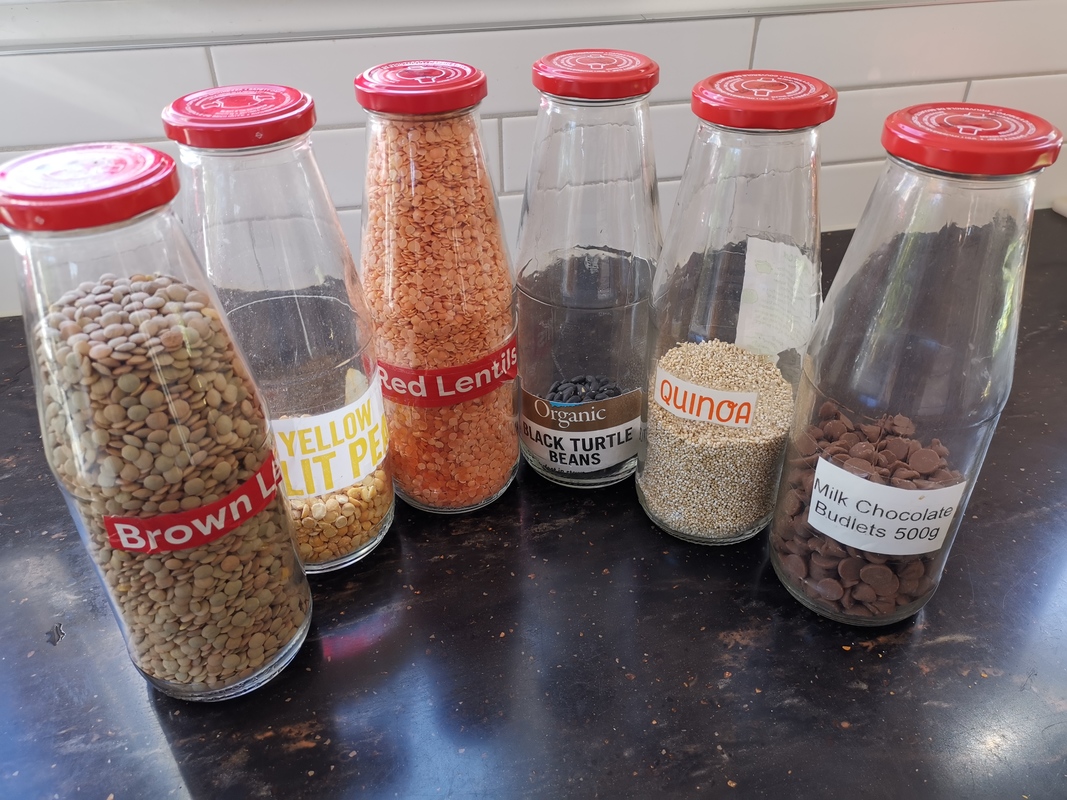 Six tall glass jars re-purposed to hold dried food items.