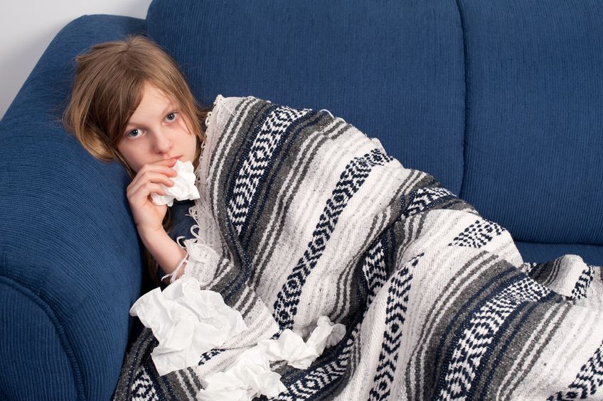 Sick child lying on blue sofa, with blanket holding tissues.