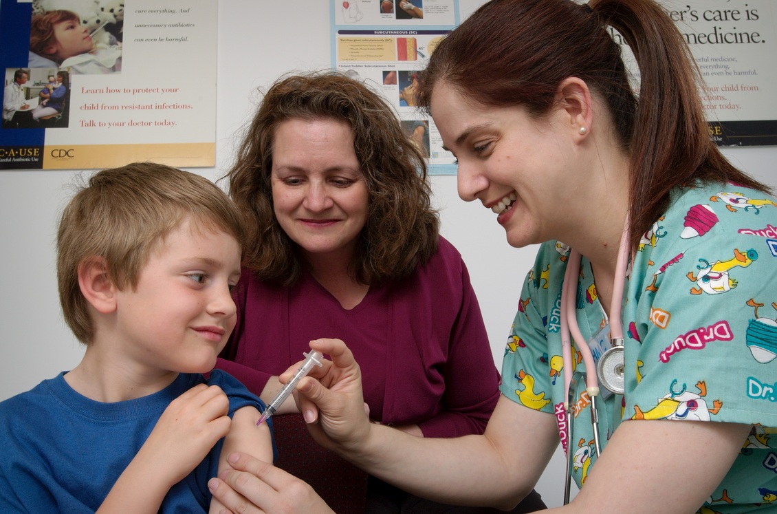 Young boy getting immunisation injection from nurse with mum