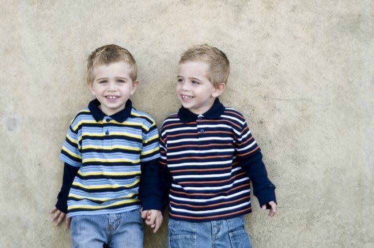 Pair of young identical twin boys leaning on a wall. 