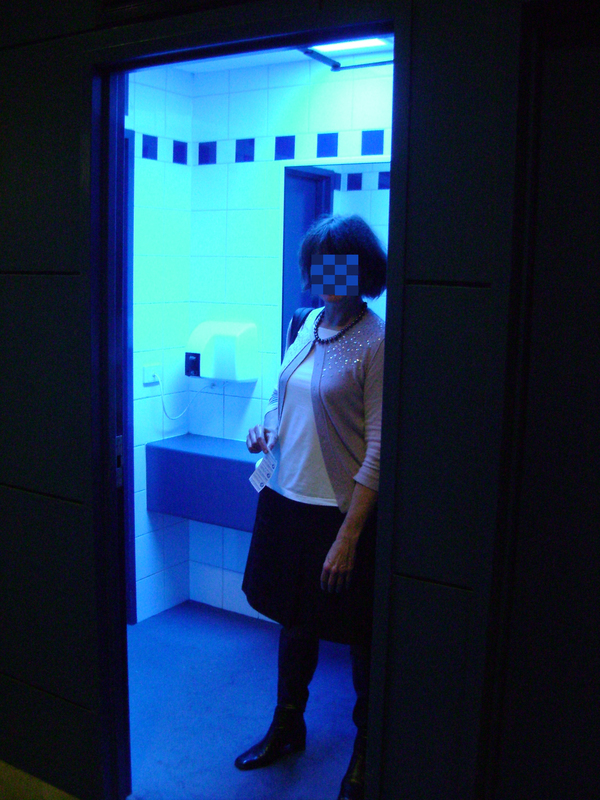 A woman standing in door of public toilet lit with UV-blue light