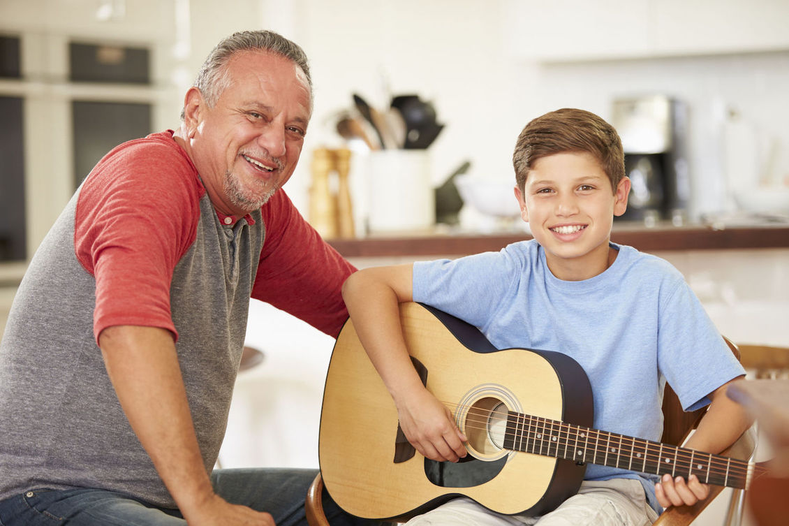 Smiling grandfather with grandson who is holding a guitar.