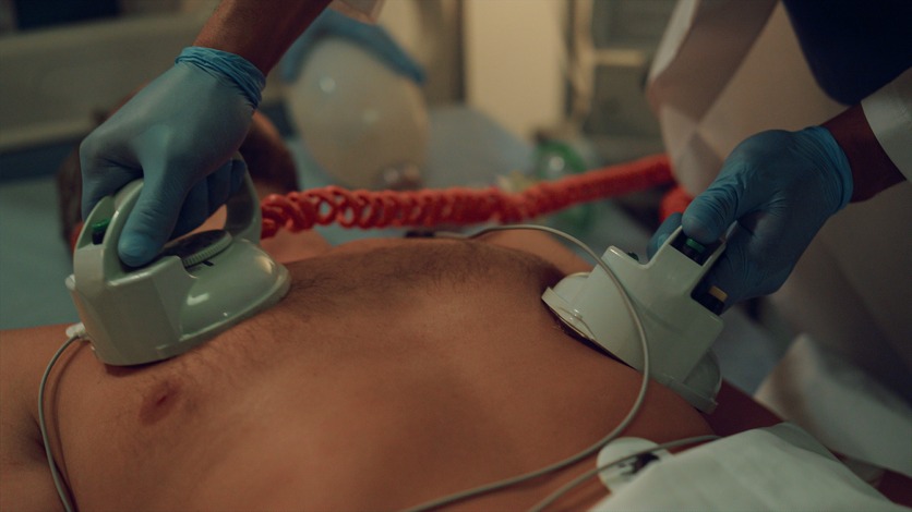 Hands holding a defibrillator to a man's chest.