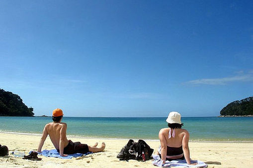 Back view of a Male and female sitting sunbathing on a beach.