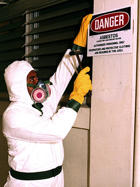 Person in protective suit putting up an asbestos warning sign