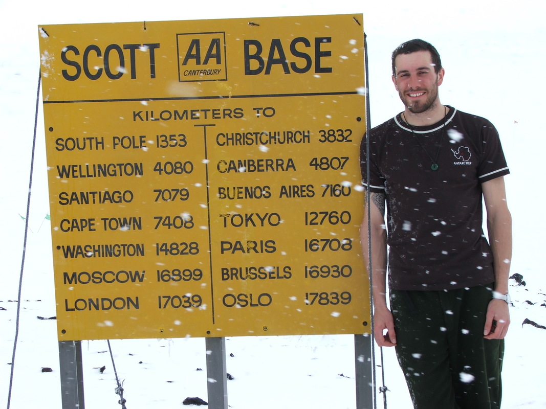 Man beside sign-post showing how far Scott Base is from cities
