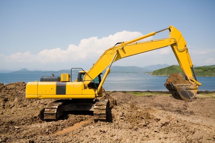 Yellow digger excavating near a coast.