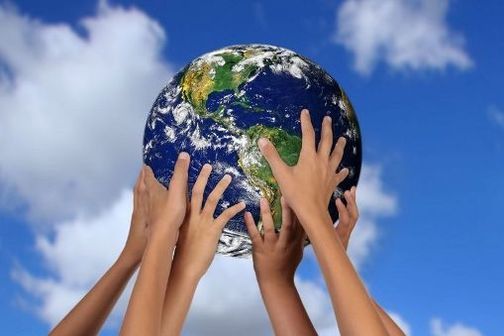 Hands holding up a globe of the Earth against a blue sky.