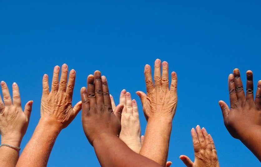 Various hands in the air with blue sky behind.