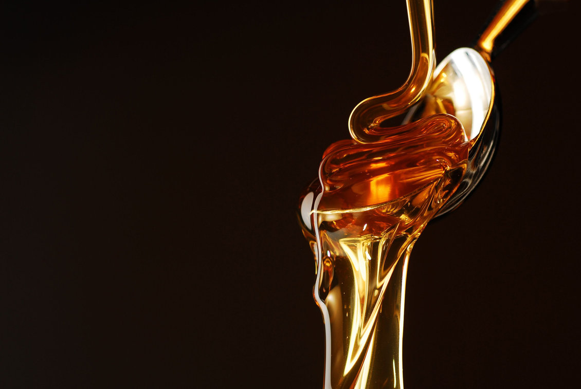 Liquid honey on a spoon with a dark background. 