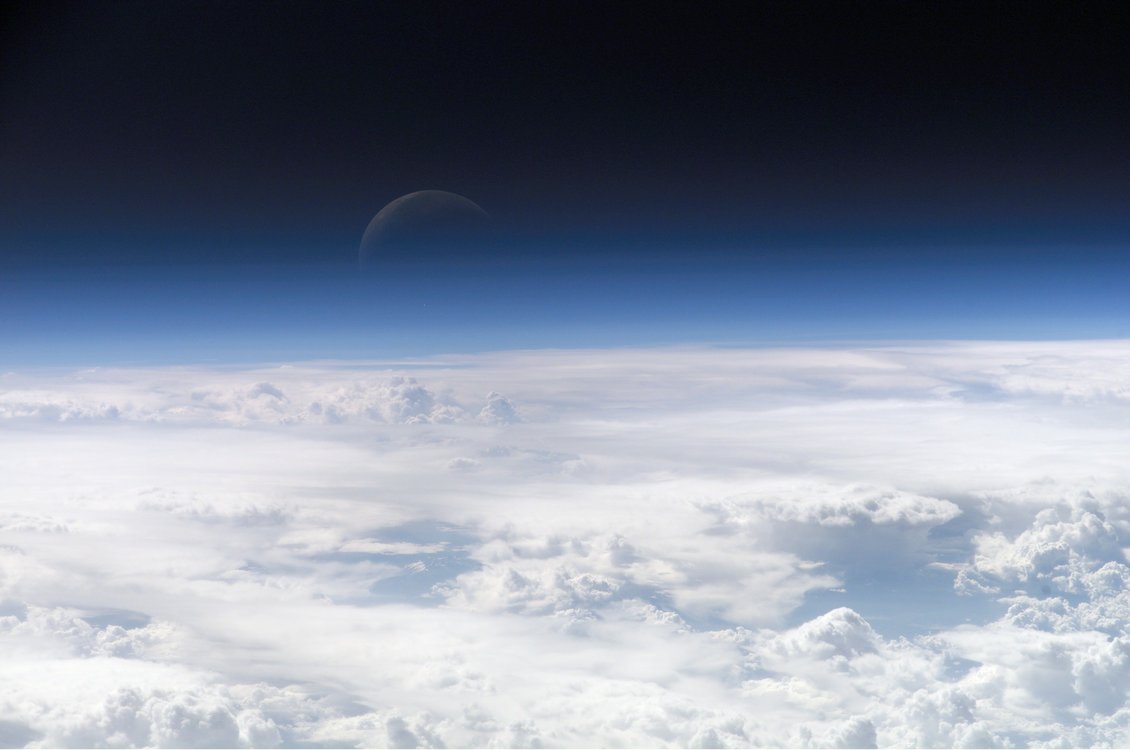 View above clouds showing atmosphere and faint moon.