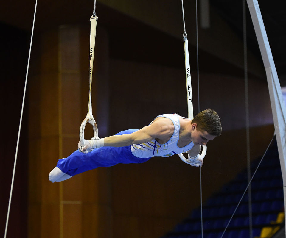 Male gymnast balancing horizontally on stationary rings.