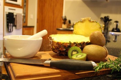 Pineapple, kiwi fruit, bowl and knife on kitchen chopping board