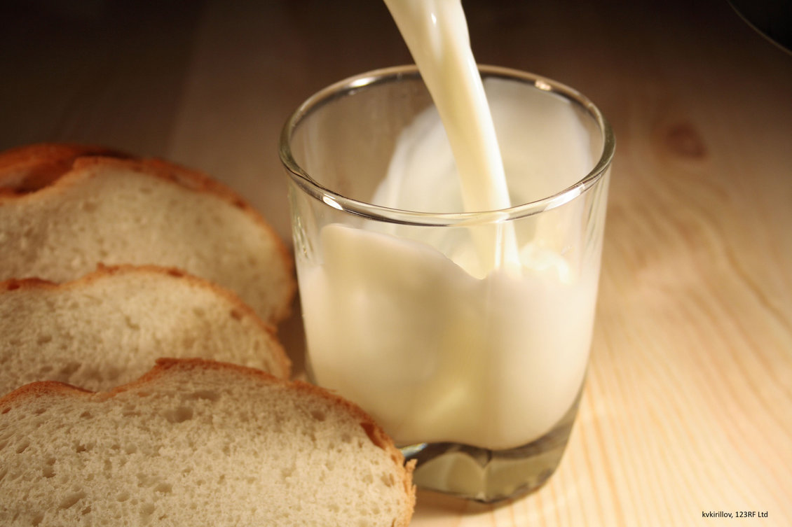 Milk being poured into a glass with slices of bread to left.