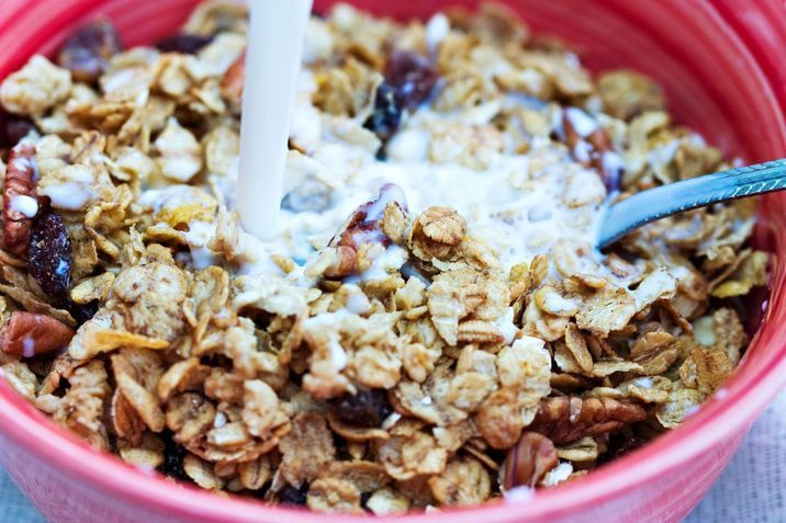 Close up of a Bowl of muesli with spoon, milk being poured in.