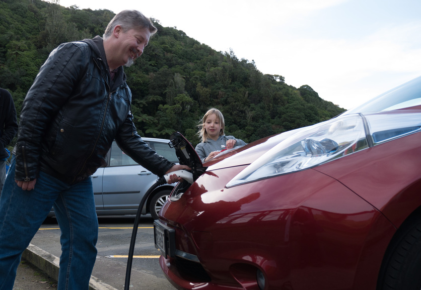 Man plugging in a red Nissan Leaf electric car to charge ourside