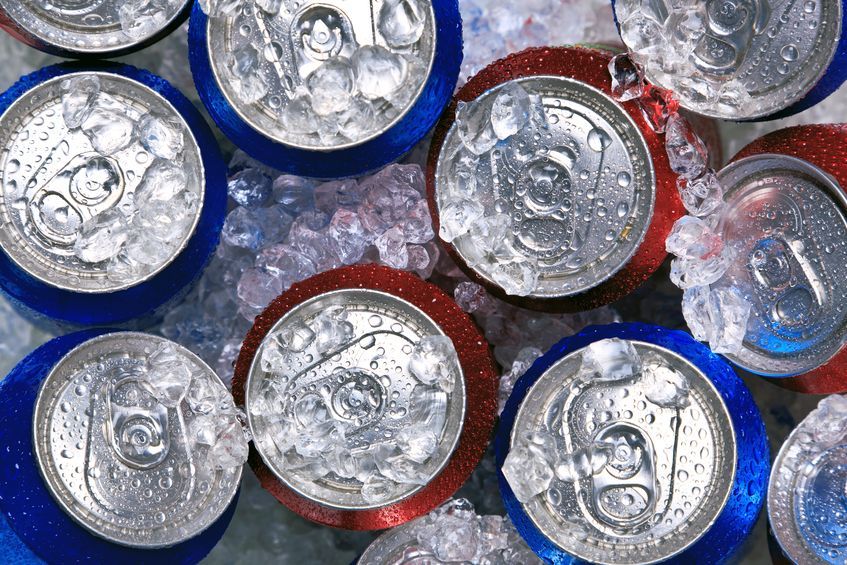 Looking down at tops of red and blue cans of soda in ice.