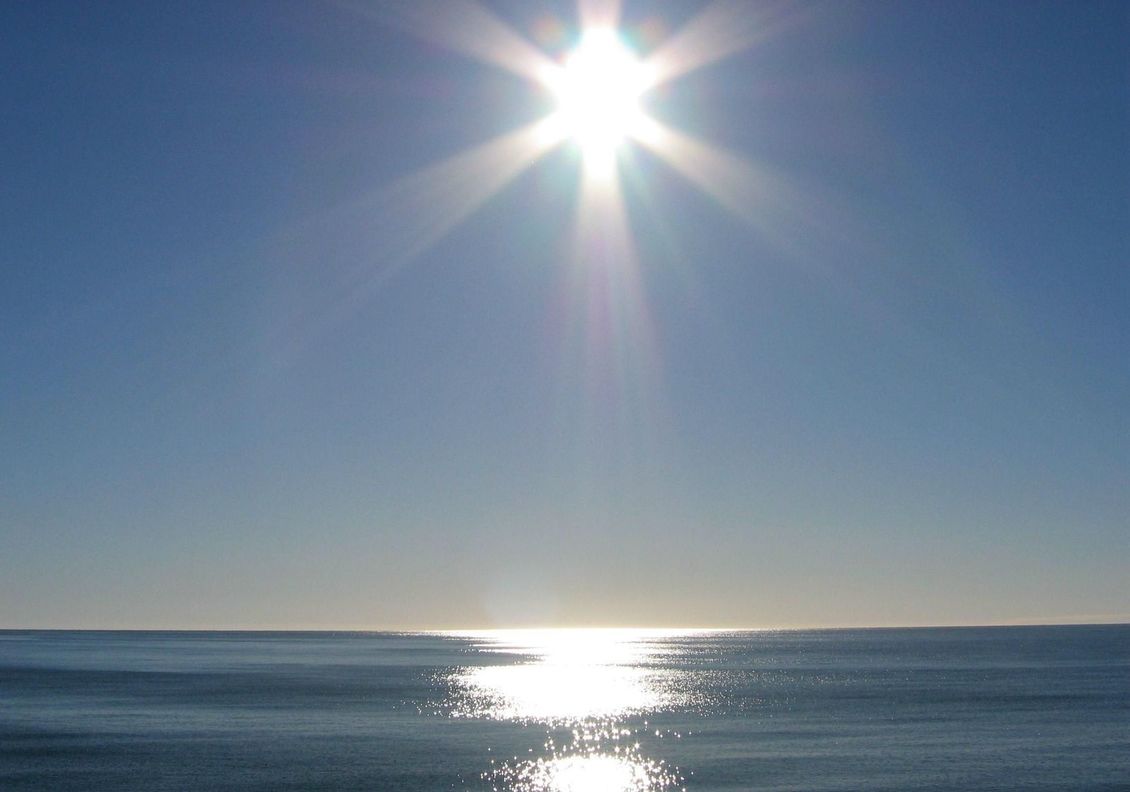Sun shining in blue sky over a still ocean. 