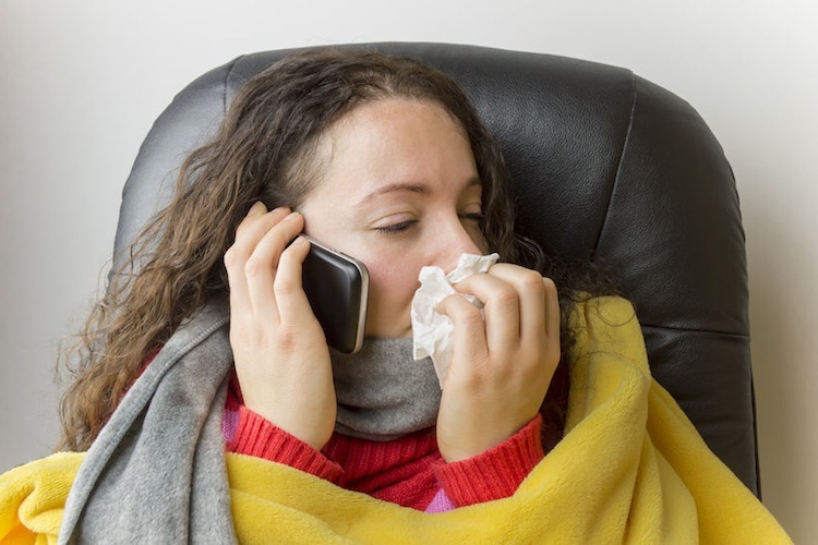 Sick woman with yellow blanket using mobile phone