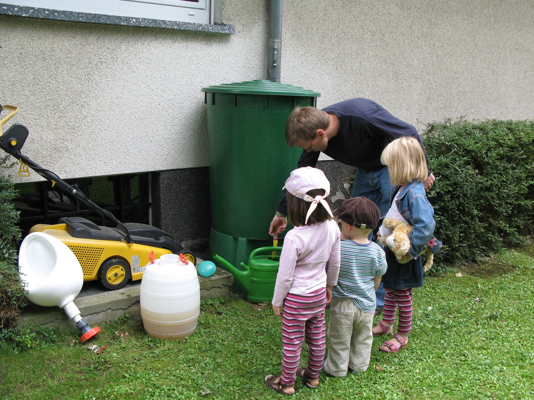 Father and 3 children in garden with rainwater tank.