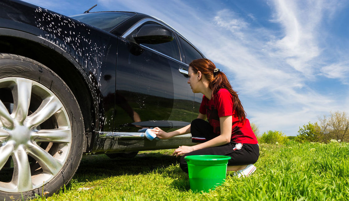 Woman washing car outside on grass.