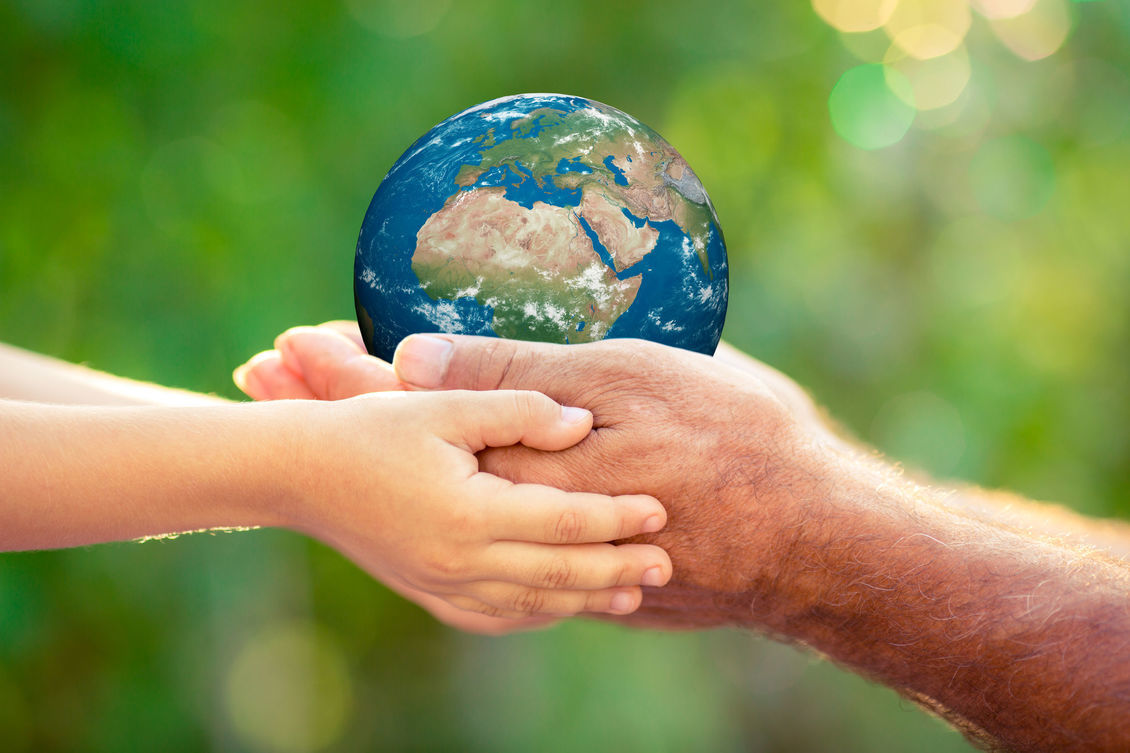 Two pairs of hands holding a small earth globe, with green back