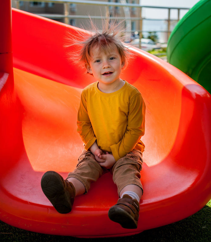 Young child at the end of an orange slide with static hair.