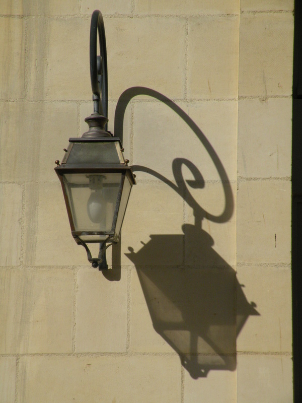 External old style lamp on stone wall casting a shadow.