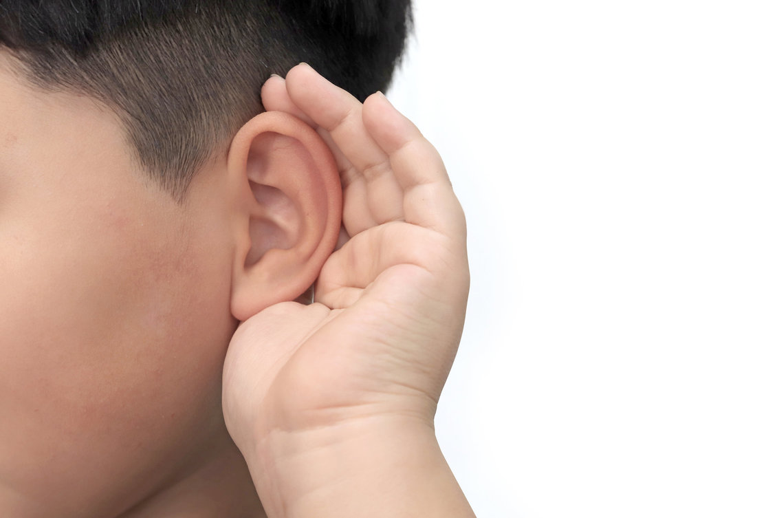 Close up of a young boy cupping his hand around his ear.