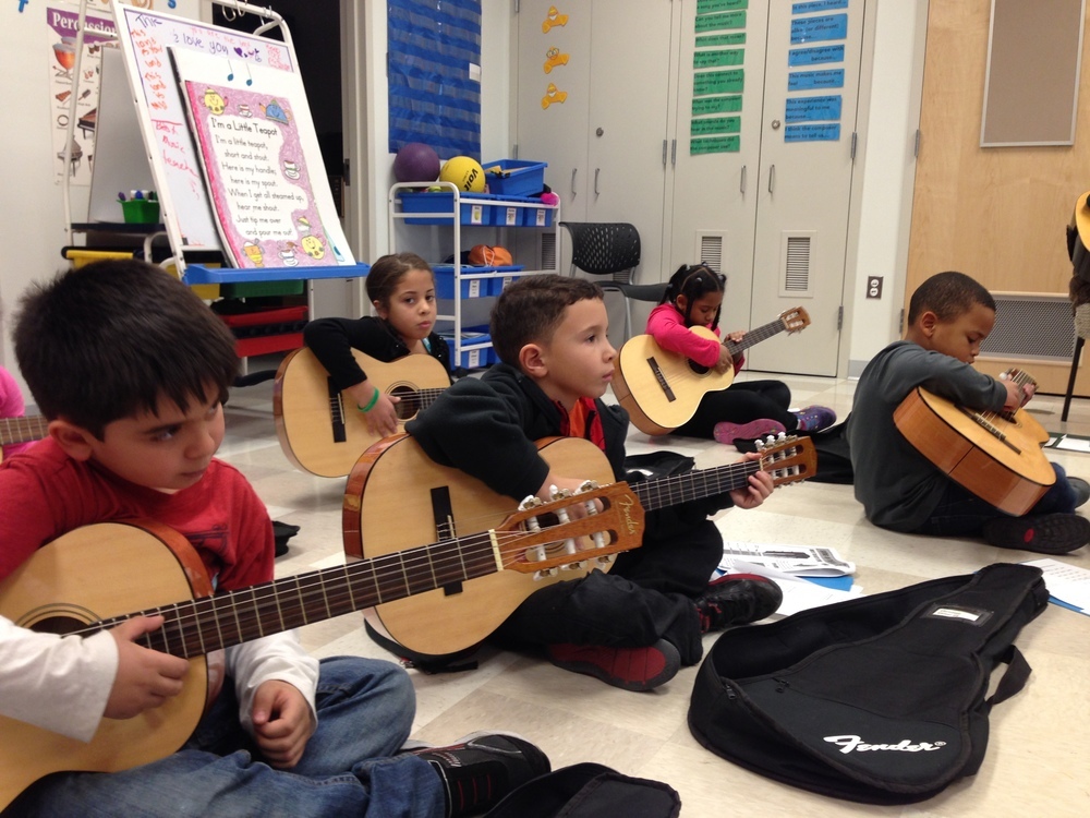Young children playing guitars in class.