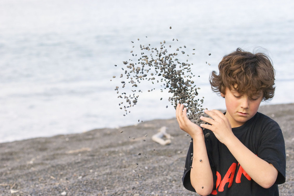 Boy throwing shingle over his shoulder at a beach.