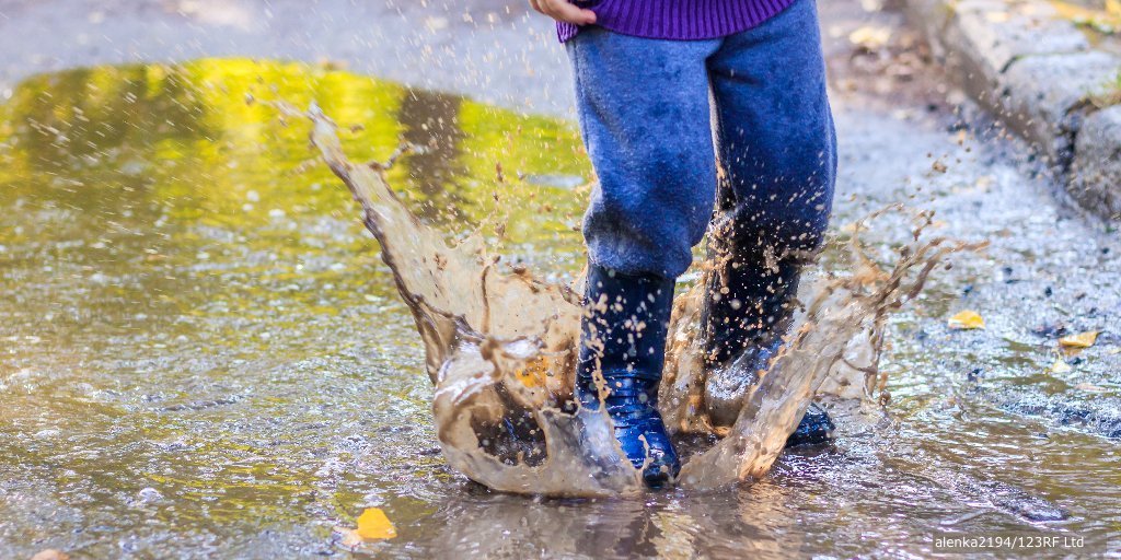 Child's wearing blue trousers & gumboots puddle splashing