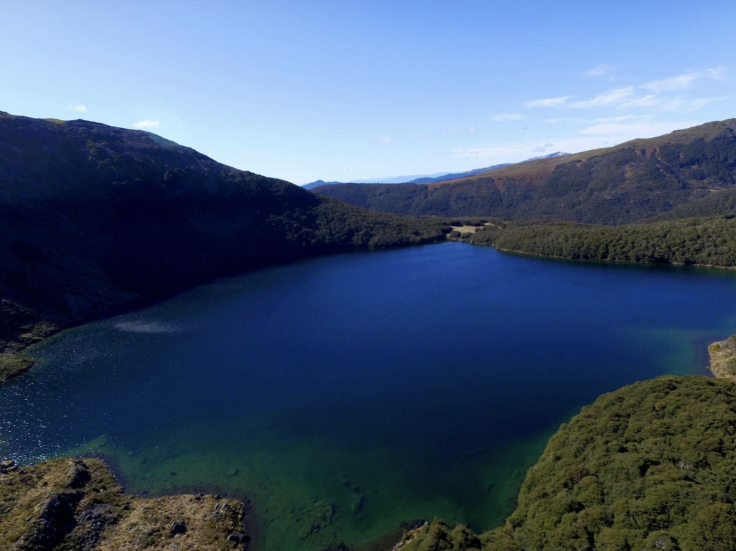 Cobalt blue lake surrounded by vegetation and steep slopes.