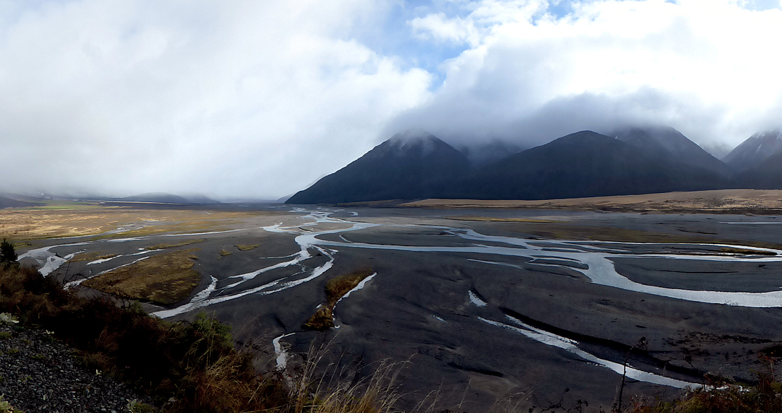  Clouds and mist cover a mountain along a braided river.