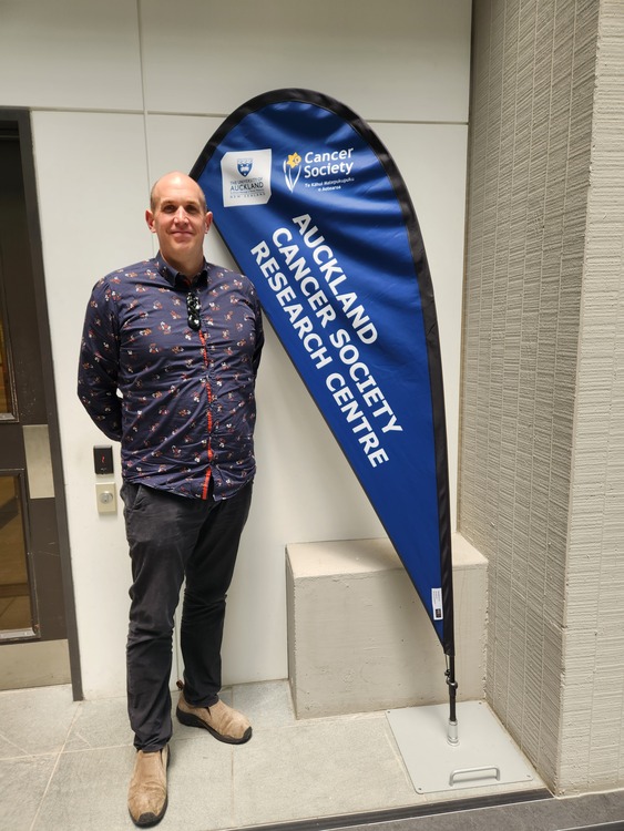Dr Kimiora Henare standing next to banner